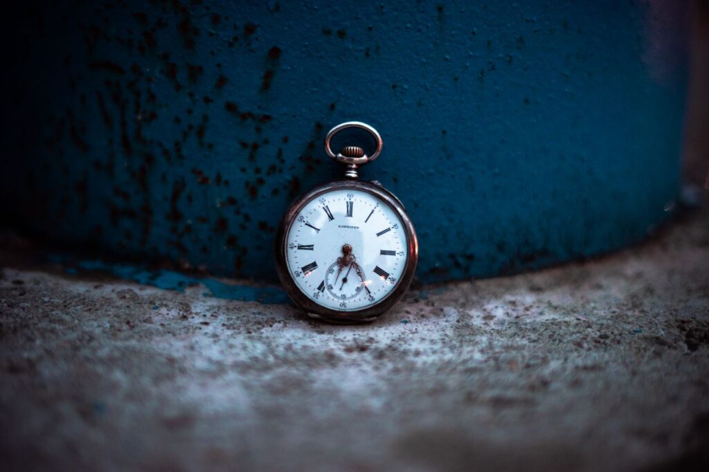 Close-up of a vintage pocket watch resting on a weathered surface with blue background.