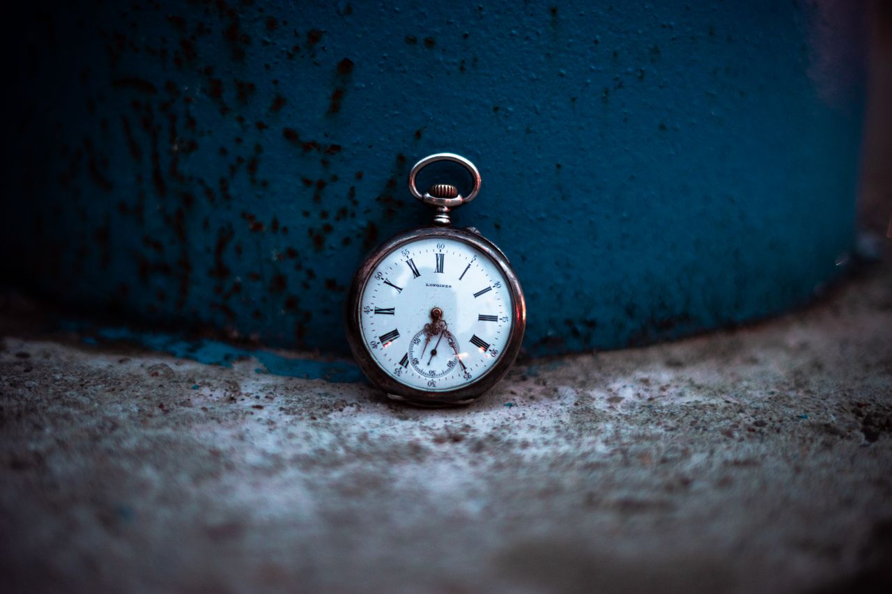 Close-up of a vintage pocket watch resting on a weathered surface with blue background.