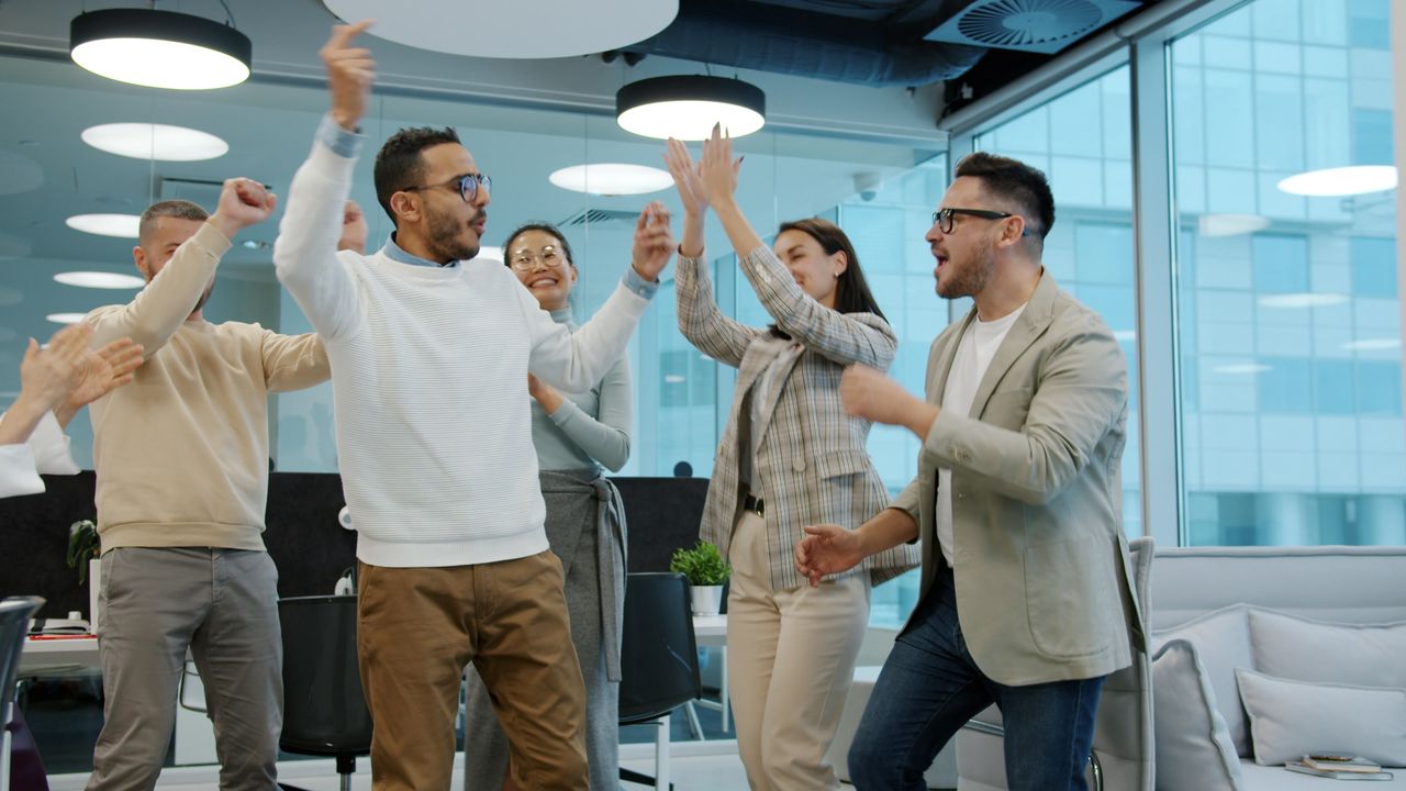 A diverse team celebrating success with enthusiasm in a modern office setting.